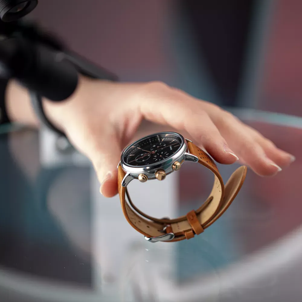 Main positionnant une montre pour homme avec bracelet en cuir marron sur une surface en verre